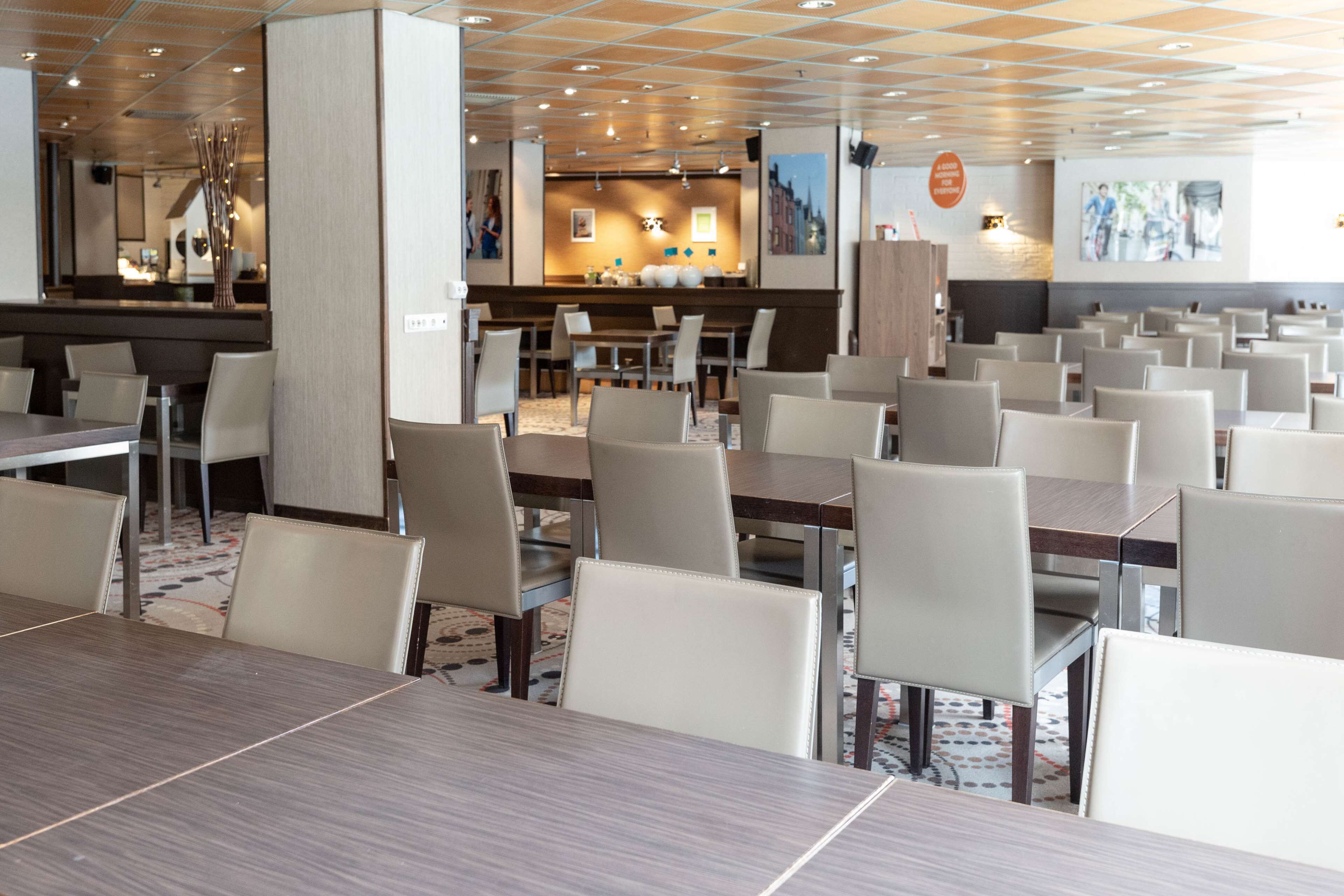 A spacious dining area with multiple tables and chairs, a central bar, and a modern ceiling design.