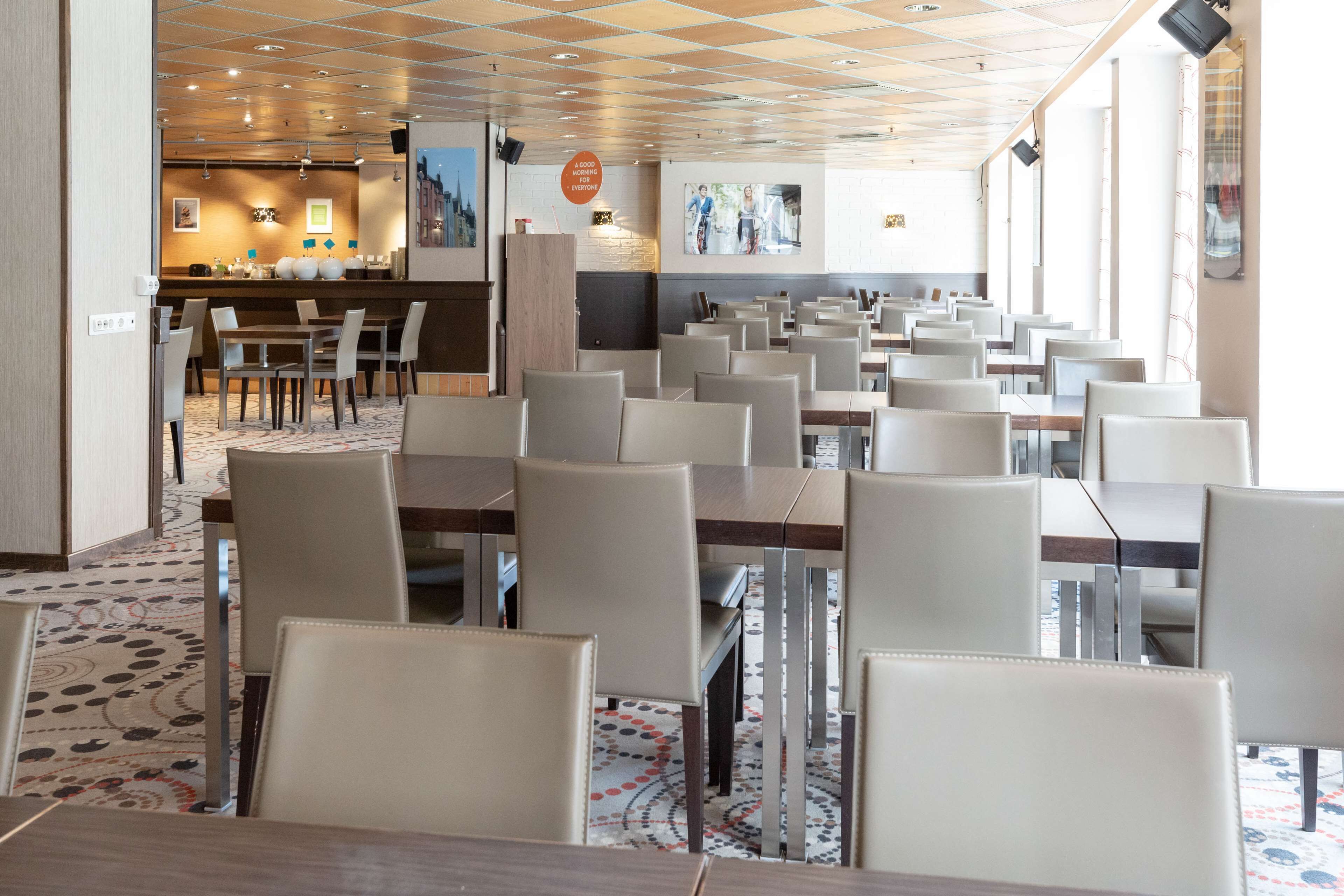Un comedor amplio con varias mesas y sillas, una zona de bar al fondo y una alfombra estampada.