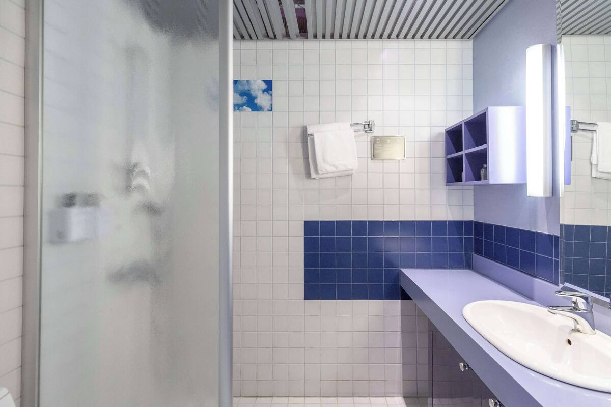 Uma casa de banho moderna com cabine de duche em vidro, lavatório branco e parede revestida a azulejos azuis.