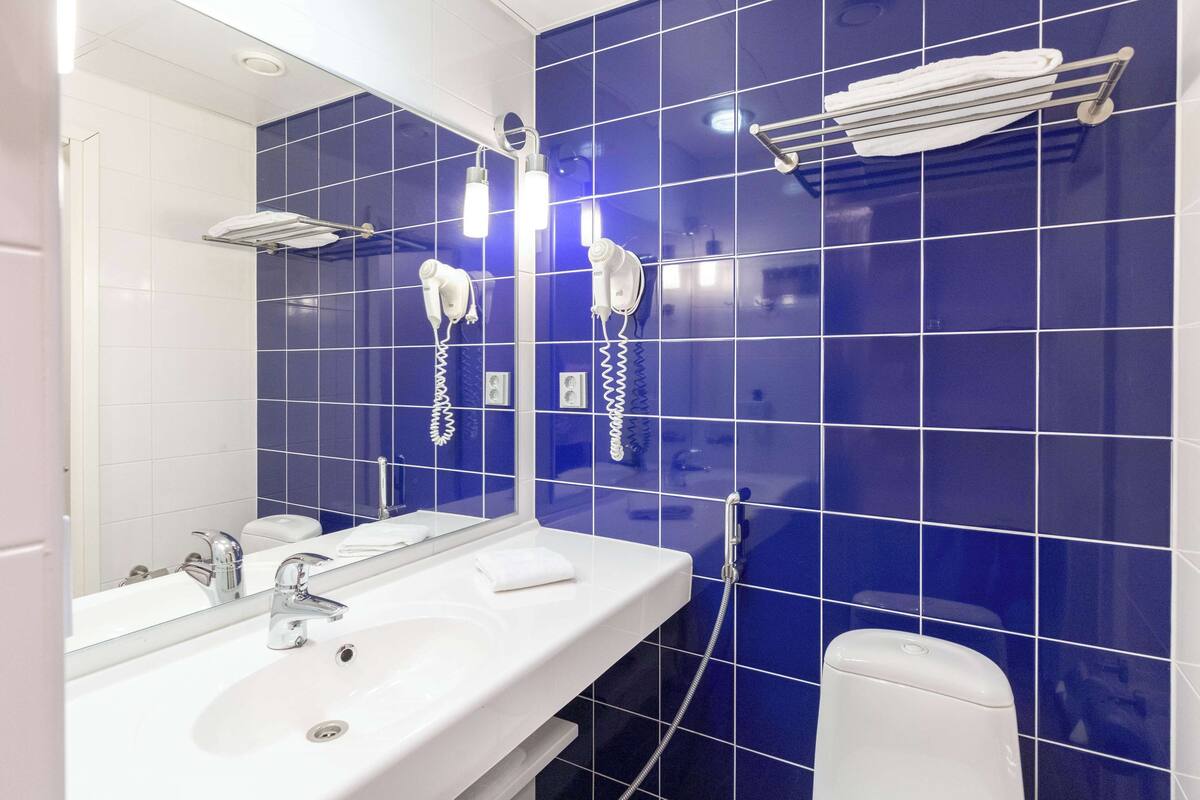 Casa de banho com uma pia branca, um espelho e dois secadores de cabelo fixados na parede.