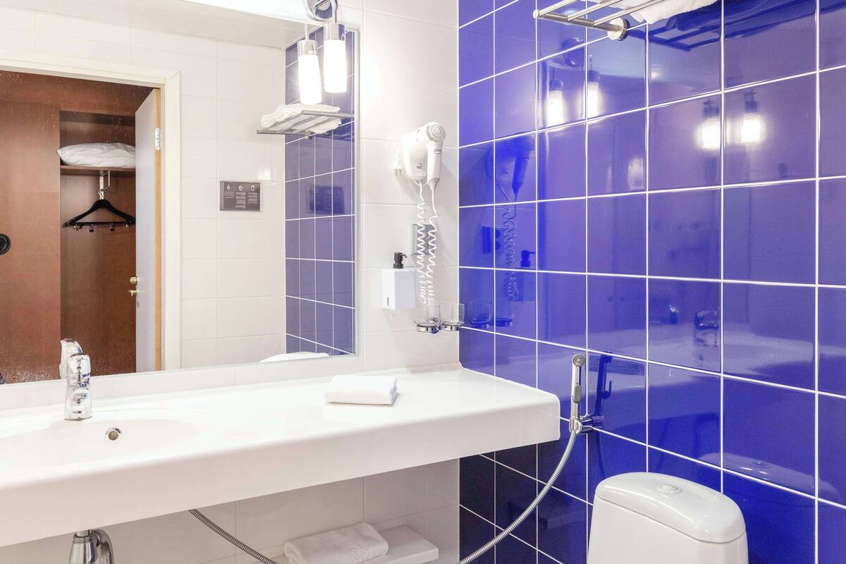 Casa de banho com uma pia branca, um espelho, um secador de cabelo e um chuveiro com azulejos azuis.