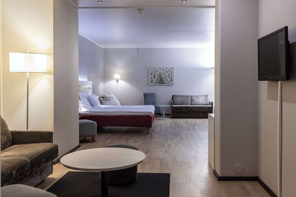 Quarto de hotel moderno com uma cama, um sofá, uma mesinha e uma televisão.