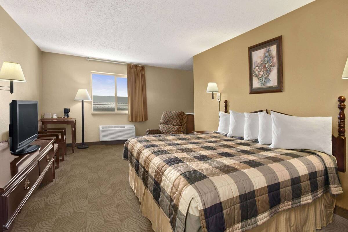Une chambre d’hôtel avec un grand lit, un bureau avec une télévision, une chaise, une fenêtre avec des rideaux et un tableau au mur.