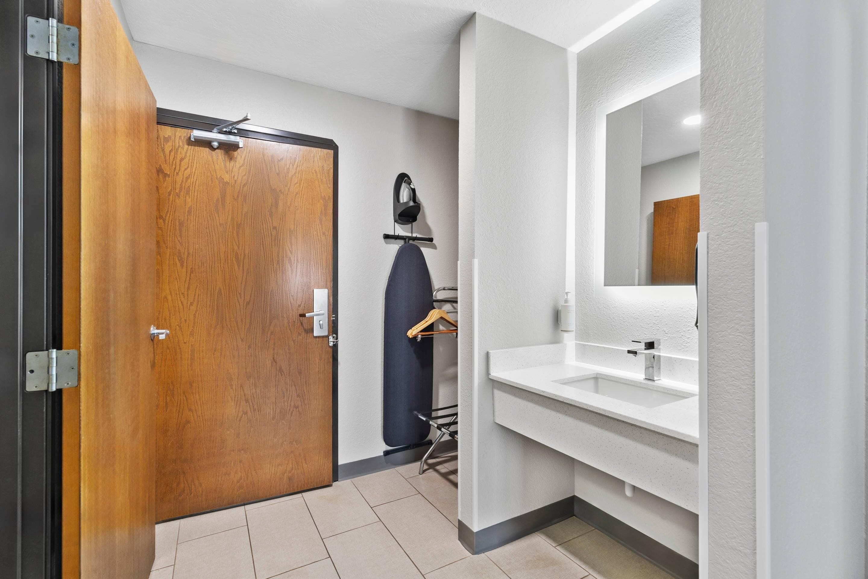 A modern bathroom with a wooden door, a white sink, and a mirror.