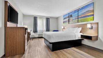 A hotel room with a bed, a TV, a desk, and a painting on the wall.
