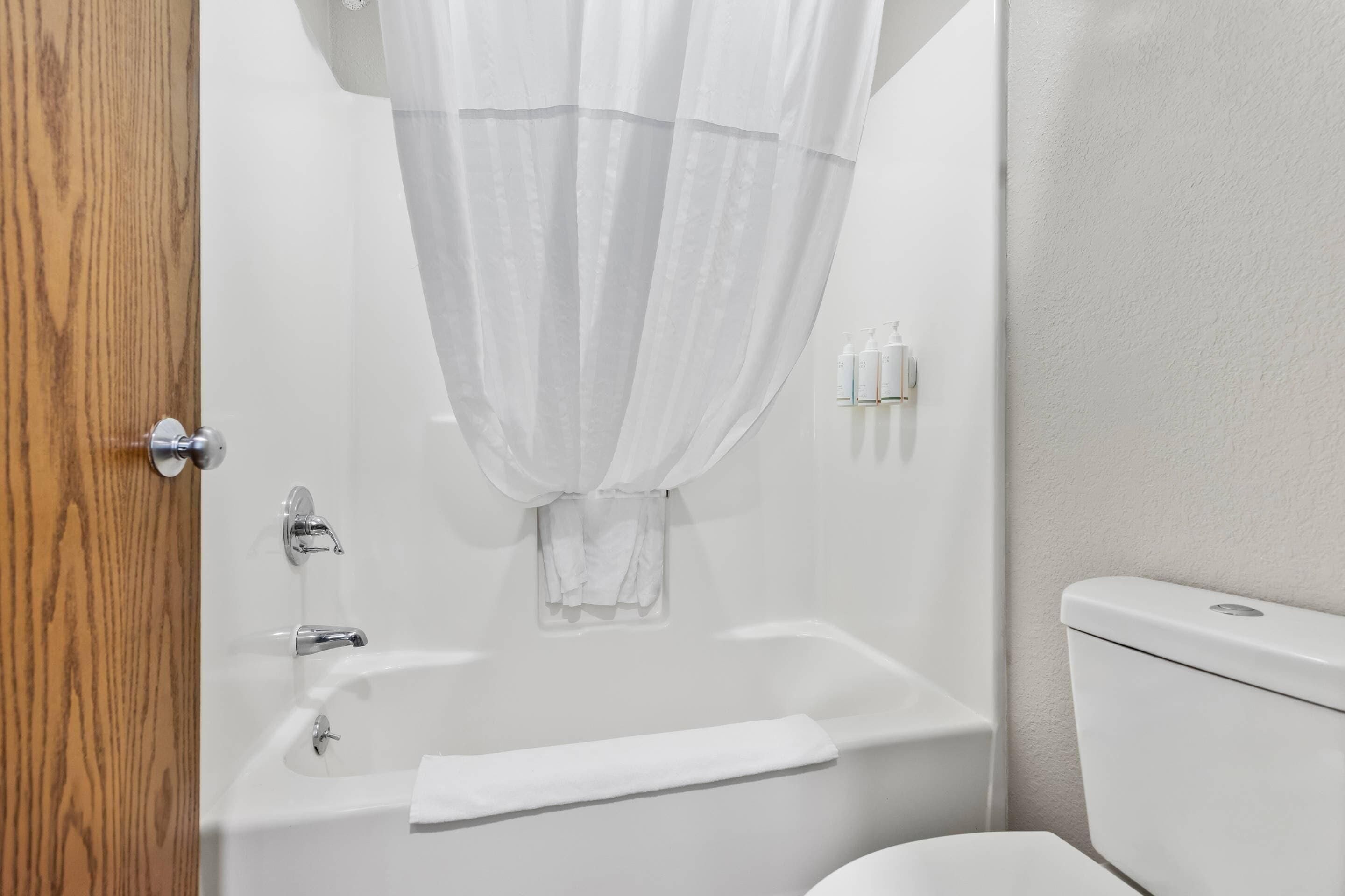 A bathroom with a bathtub, toilet, and a wooden door.