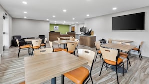 Un espace repas moderne, doté de plusieurs tables et chaises, d’un comptoir d’accueil et d’un téléviseur à écran plat fixé au mur.