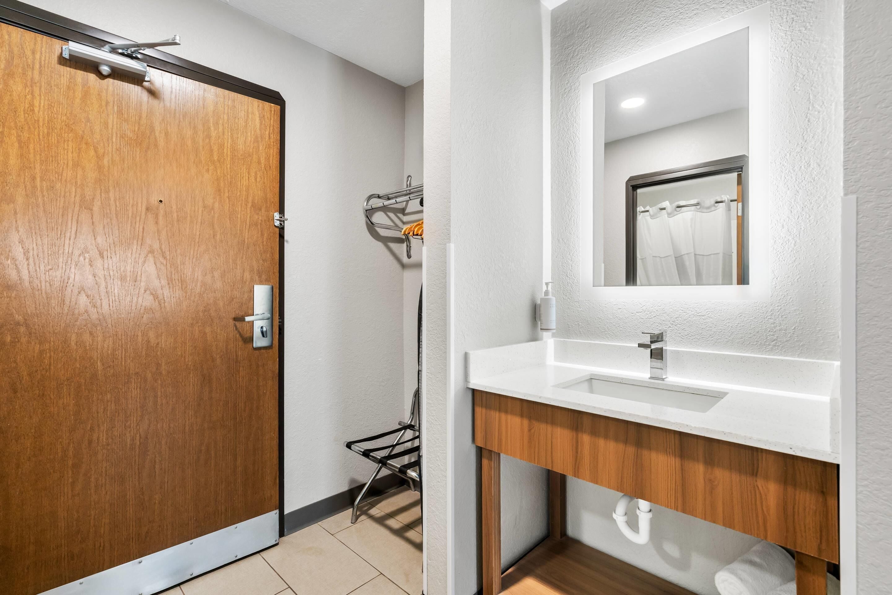 Un baño moderno con una puerta de madera, un lavabo blanco y un espejo.