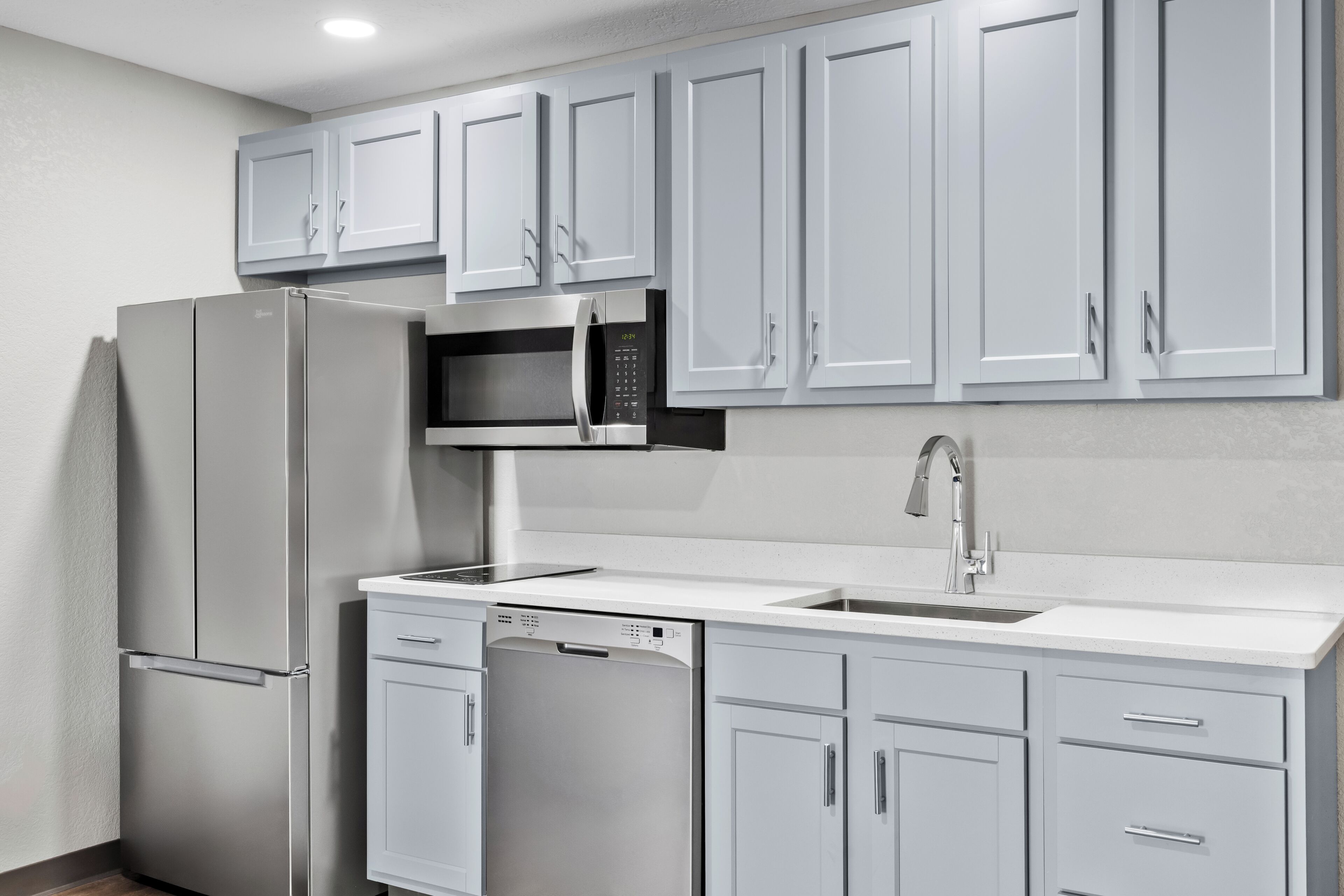 A kitchen with white cabinets, a stainless steel refrigerator, a microwave, a dishwasher, and a sink.