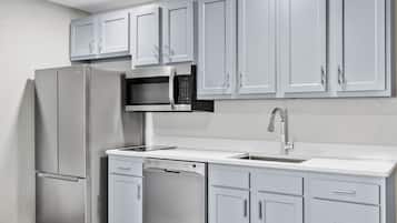 A kitchen with white cabinets, a stainless steel refrigerator, a microwave, a dishwasher, and a sink.