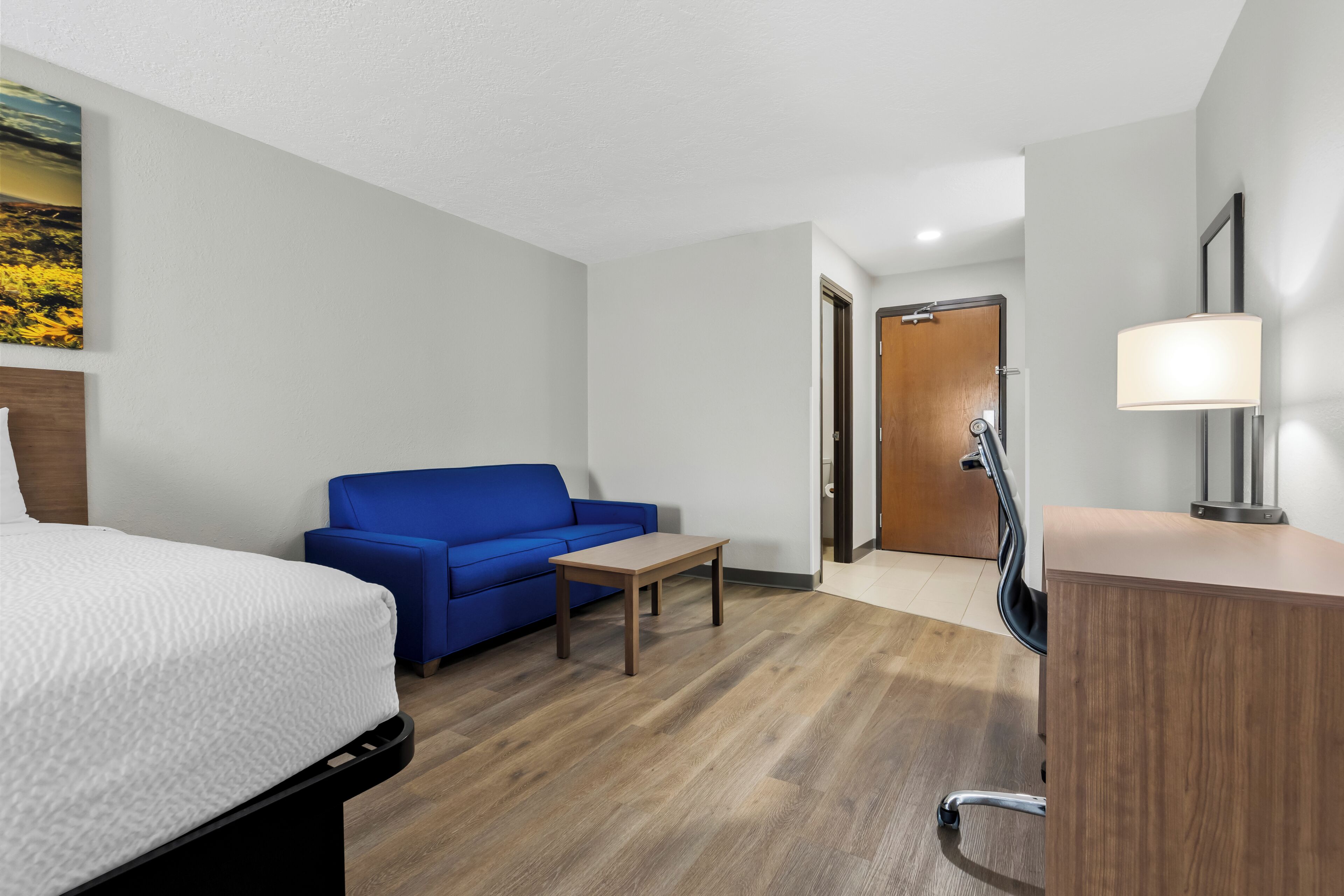Habitación de hotel con una cama, un sofá azul, una mesita, un escritorio y una lámpara.