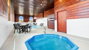 Un espace piscine doté d’un jacuzzi, d’un plafond en bois et d’un coin repas avec chaises et tables.