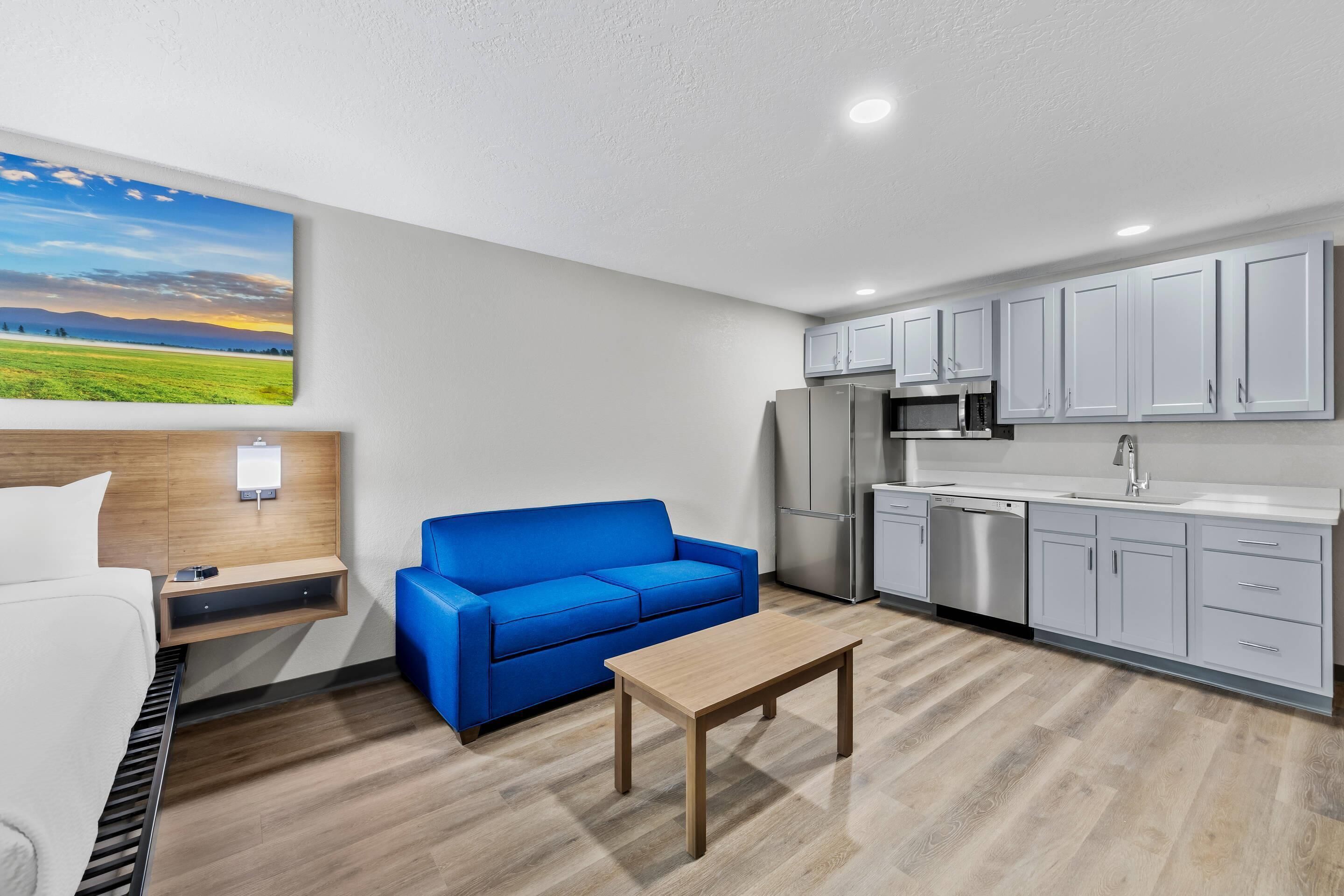 A modern kitchenette with stainless steel appliances, a blue sofa, and a wooden table.