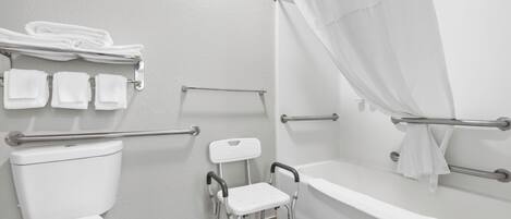 Un baño con inodoro blanco, ducha con cortina, barra de apoyo y un taburete pequeño.