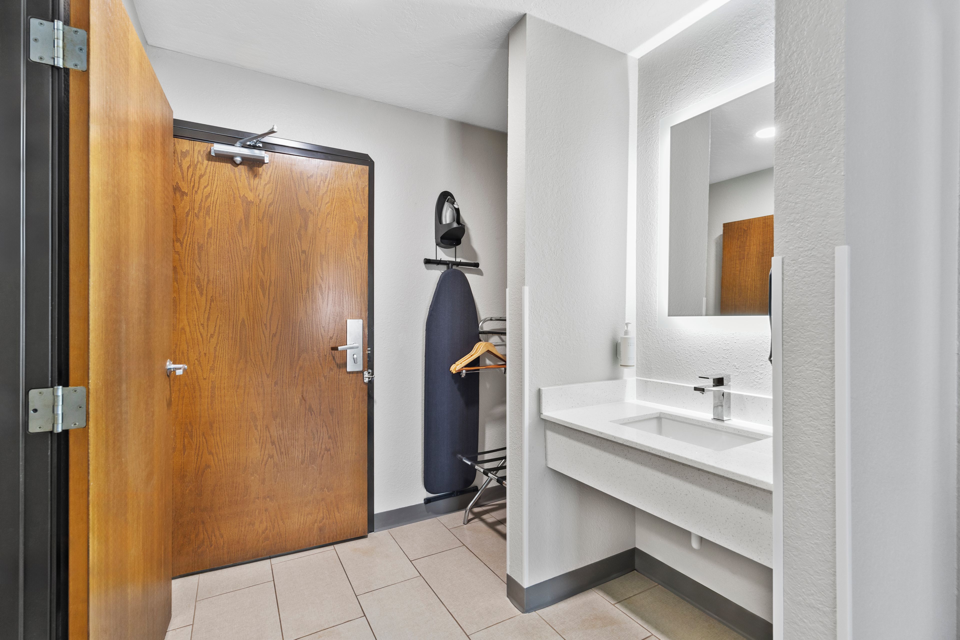 A modern bathroom with a wooden door, a white sink, and a mirror.