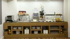 Un bufé de desayuno con diversas opciones de comida, una máquina de café y una presentación de frutas.