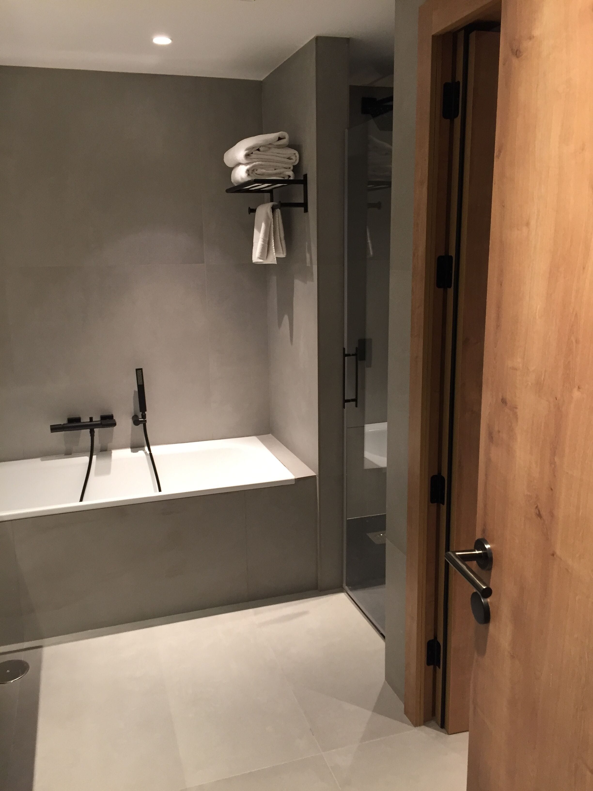 Un bagno moderno con una vasca da bagno indipendente, un porta asciugamani con asciugamani piegati e una porta in legno.