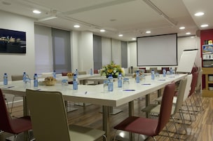 Ein Konferenzraum mit langen Tischen, Stühlen, Wasserflaschen, einer Projektionsleinwand und einer Whiteboard-Tafel.