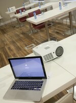 A laptop on a table with a projector in front of it.