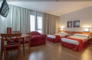 Ein Hotelzimmer mit zwei Betten, einem Esstisch und Stühlen.