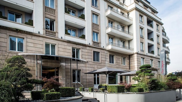 Un hotel de varios pisos con fachada moderna, balcones y un área exterior bien cuidada, con escalones y vegetación.