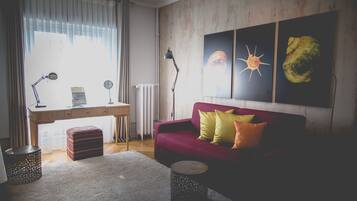 A room with a wooden desk, a red sofa, and a wall with three framed artworks.