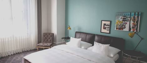 A neatly arranged hotel room with a bed, a chair, a nightstand, and a lamp.