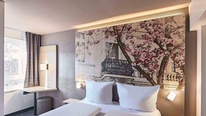A hotel room with a bed, bedside tables, a desk, and a large floral mural on the wall. - B&B Hotel Bonn-City (Bonn)