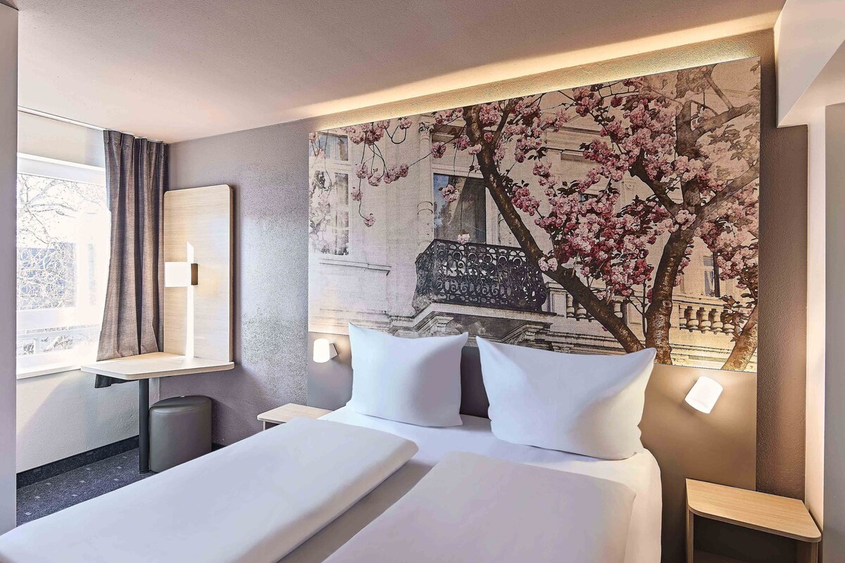 A hotel room with a bed, bedside tables, a desk, and a large floral mural on the wall.