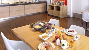 A breakfast setting with a wooden table, white chairs, and a variety of breakfast items including fruits, pastries, and beverages. - B&B Hotel Bonn-City (Bonn)