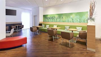 Un interior moderno con zonas de estar, un mostrador de recepción y una pared verde con la palabra 'RENDEZVOUS' escrita en ella.