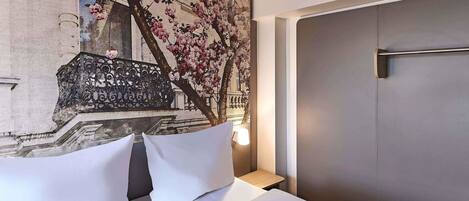 Habitación de hotel con cama, almohadas, mesita de noche, lámpara y un mural en la pared que muestra un edificio con cerezos en flor.