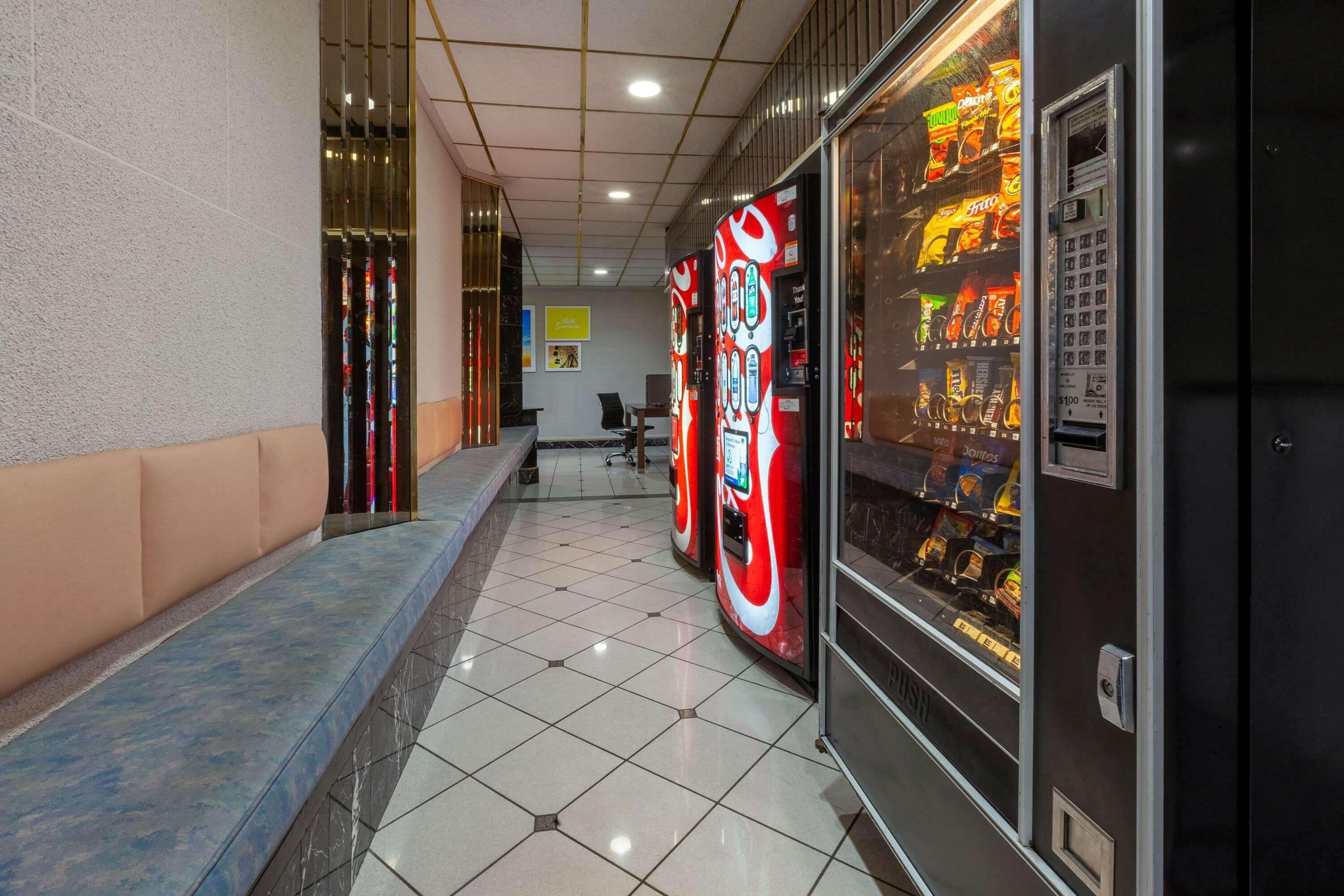 A hotel corridor with vending machines, a seating area, and a reception desk.
