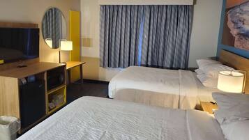 A hotel room with two beds, a TV, a desk with a lamp, and a window with curtains.