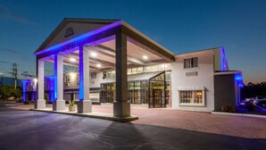 A modern hotel with a covered entrance, large windows, and a well-lit facade.