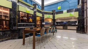 A hotel lobby with a marble reception desk, a dining area with a wooden table and chairs, and a large aquarium.