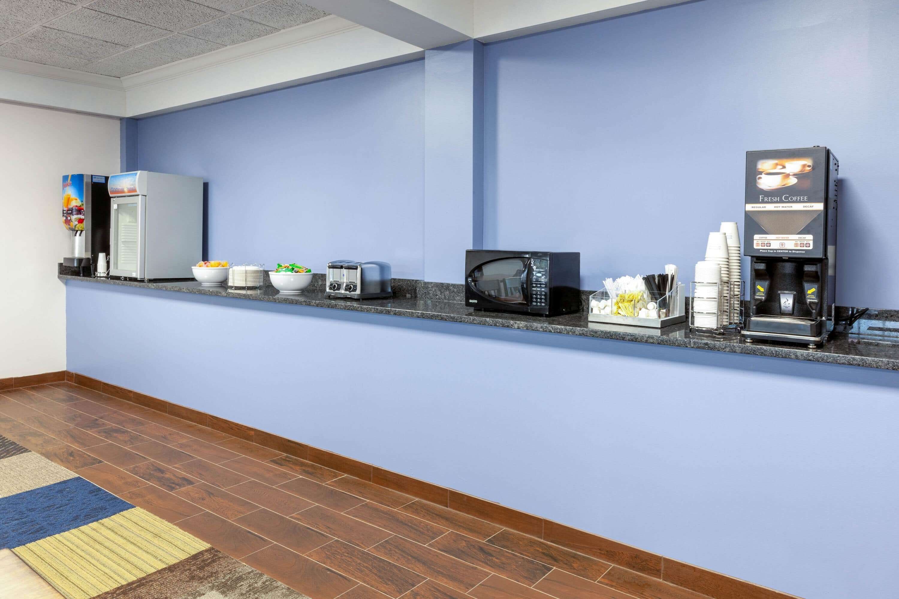 A hotel reception area with a blue wall, a coffee machine, a microwave, and various food items on a counter.