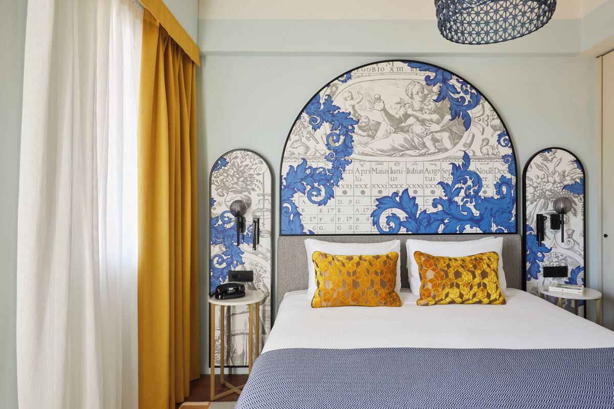 Habitación de hotel con una cama grande, dos almohadas, una mesita de noche, un espejo y un cabecero decorativo.