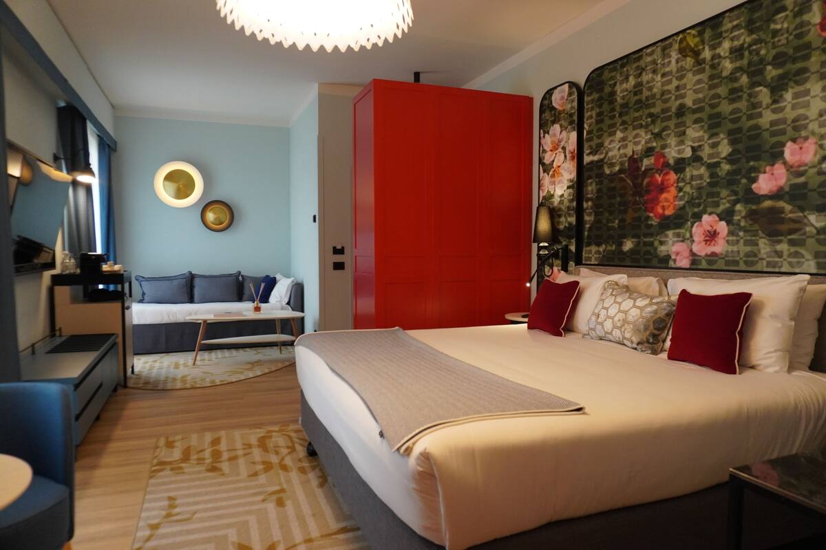 Un dormitorio moderno con una cama grande, un armario rojo, un sofá y un mural floral.