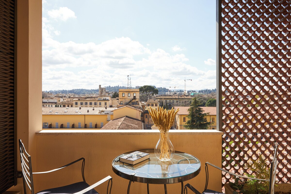 A balcony with a glass table, a chair, and a vase with dried plants.