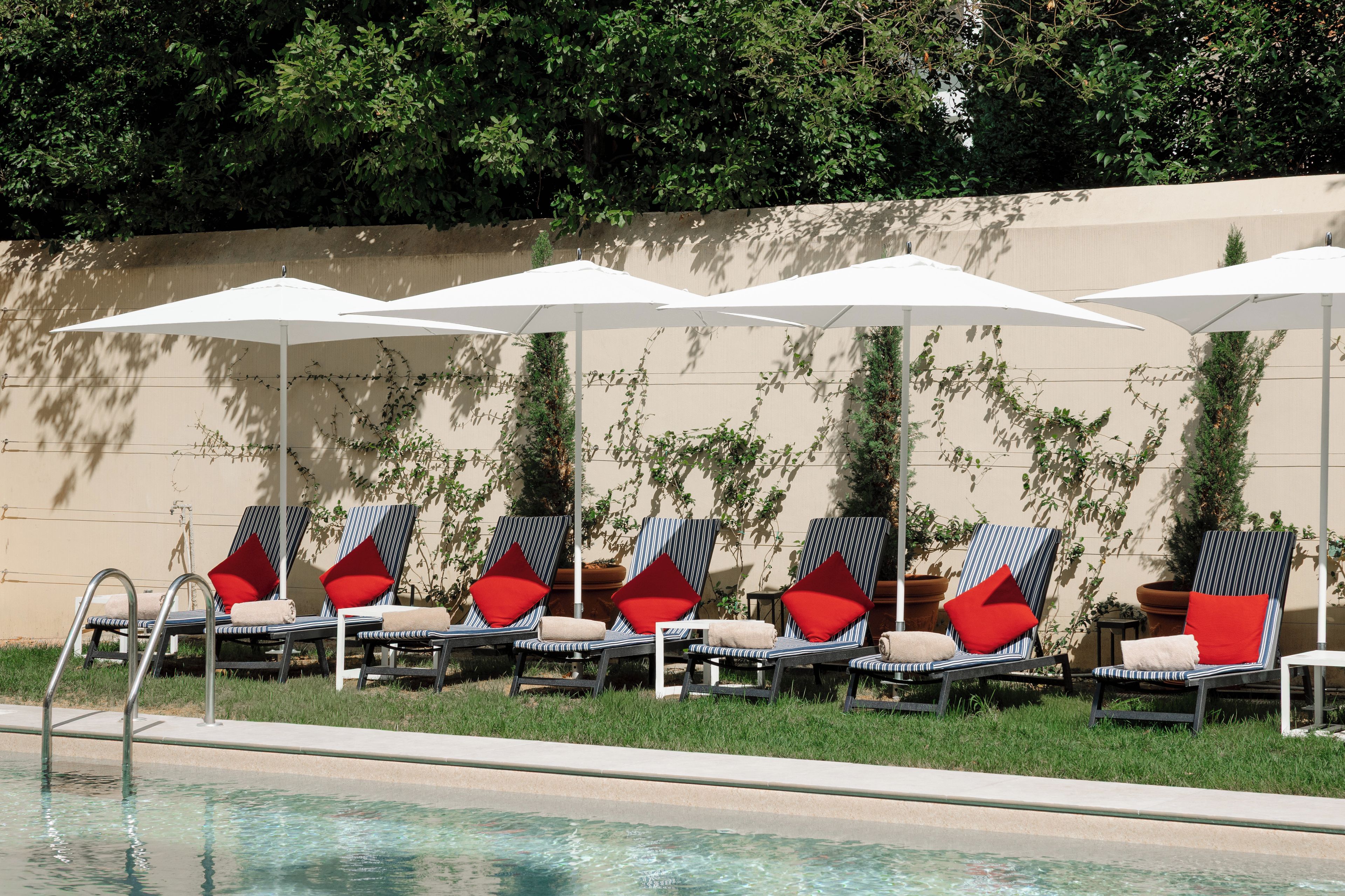 Un espace aménagé au bord de la piscine, avec des chaises longues et des parasols, une piscine, et un mur recouvert de plantes grimpantes.