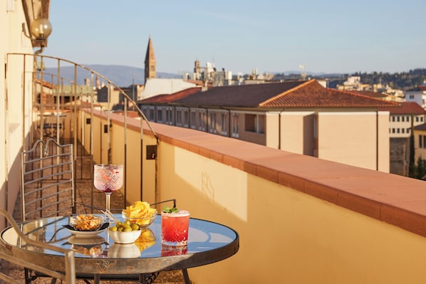 A balcony with a table set for two, featuring a drink and a bowl of olives.