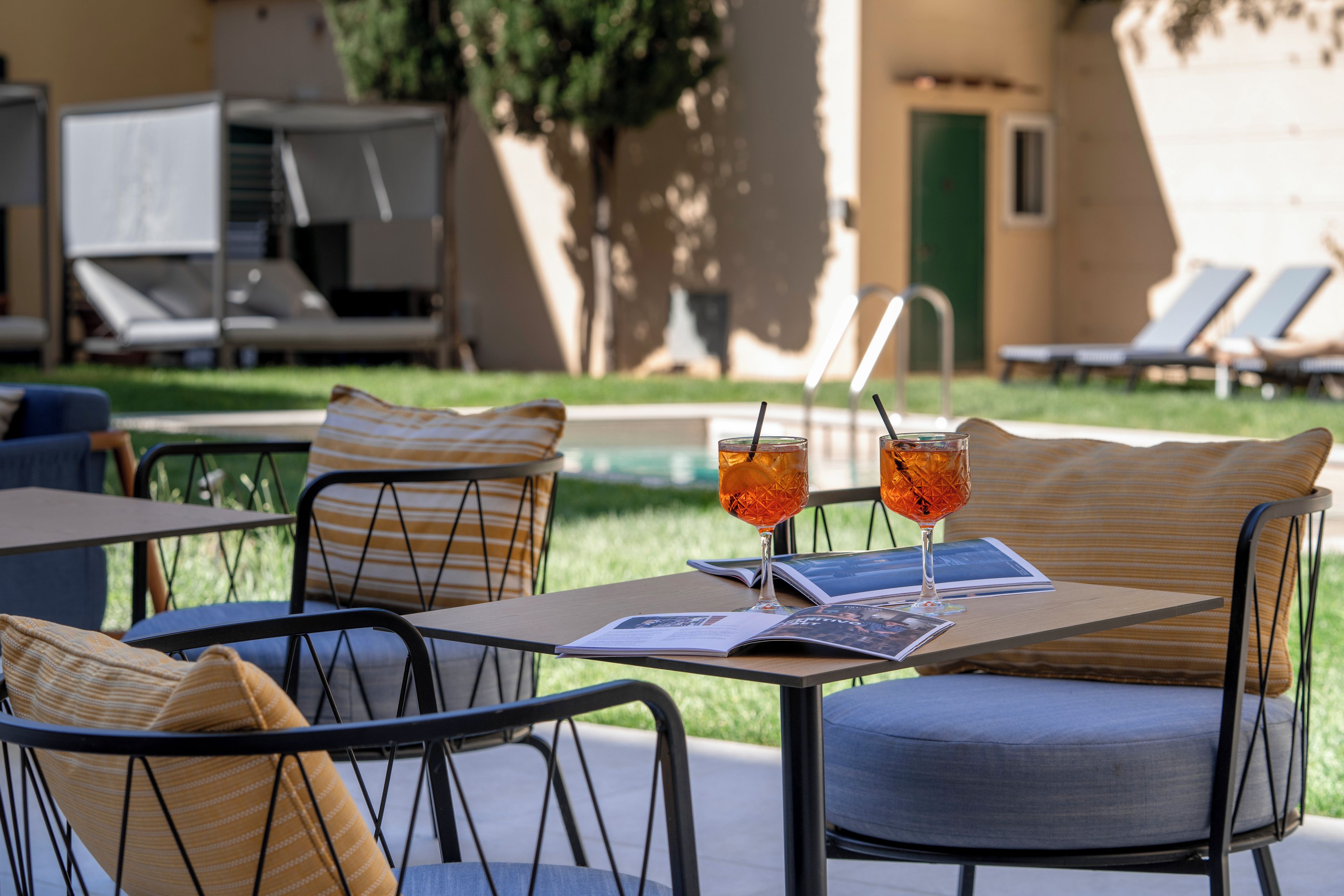 Un área de descanso junto a la piscina con sillones reclinables y una mesa con bebidas y una revista.