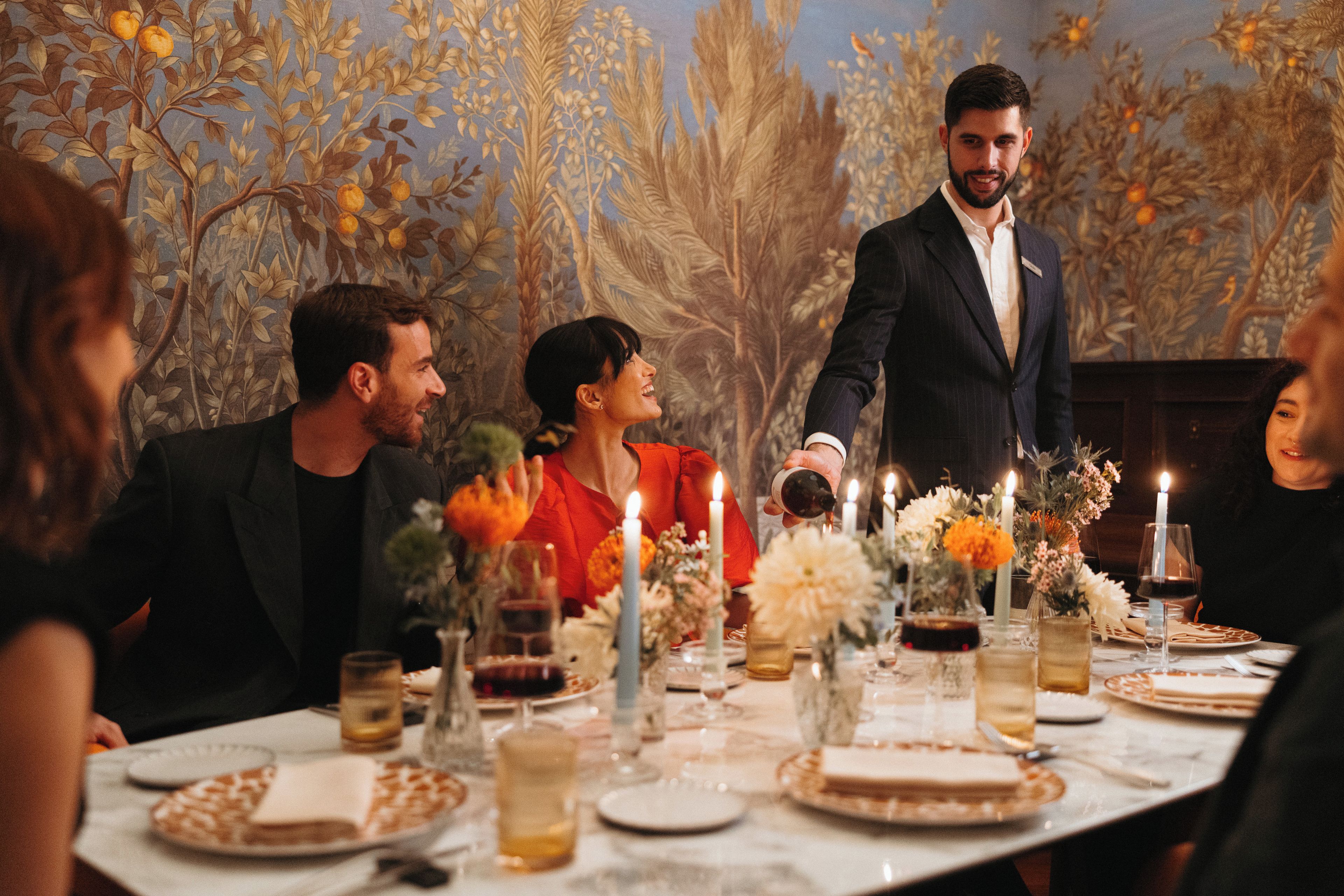 Un grup de persones assegudes al voltant d'una taula amb espelmes i decoracions florals, cosa que suggereix un ambient de sopar formal.
