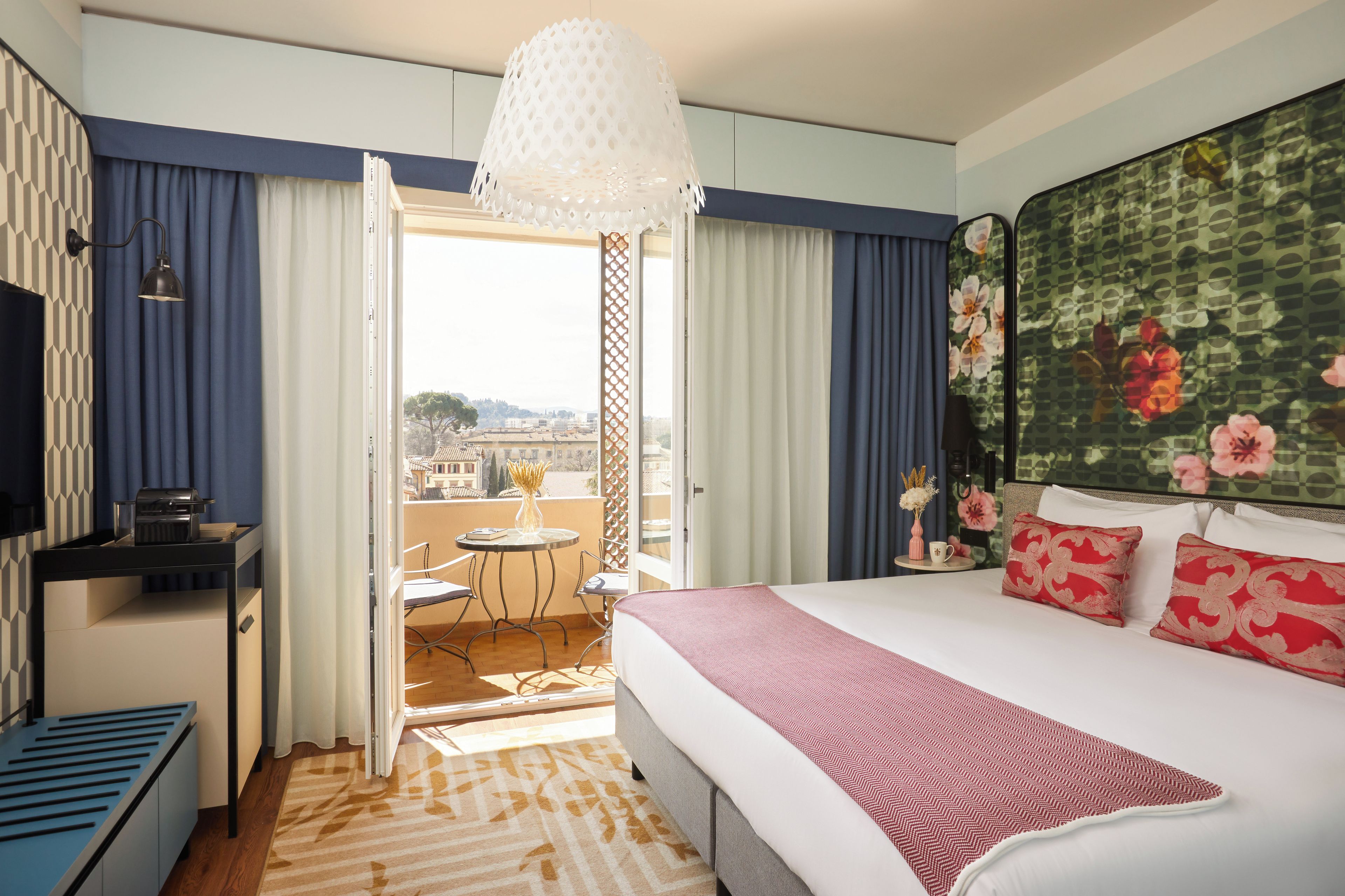 A hotel room with a bed, a desk, a chair, a table, and a balcony with a view.