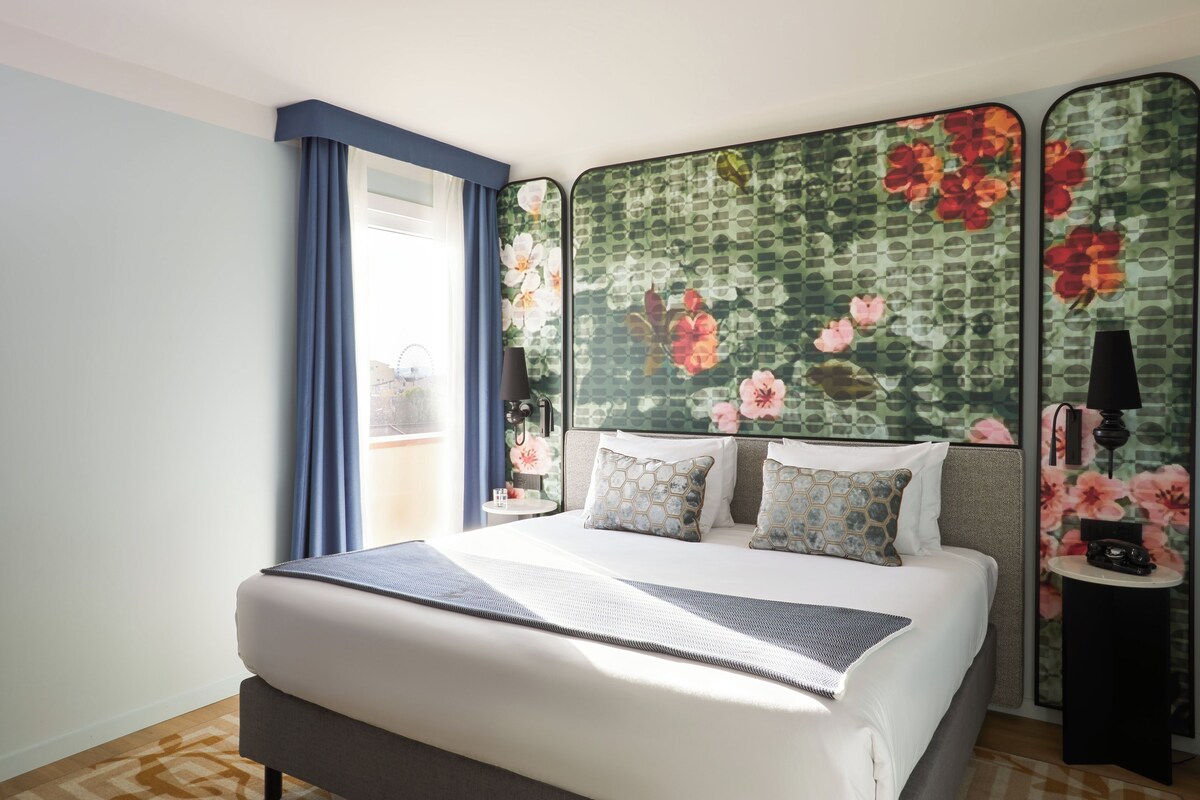 A hotel room with a large bed, a view of the city, and a decorative headboard.