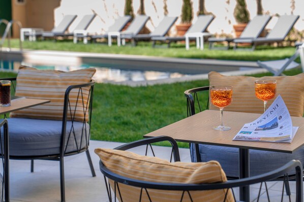 Un espace aménagé au bord de la piscine, avec des chaises longues et une table où sont servis des boissons et où l’on peut consulter le menu.