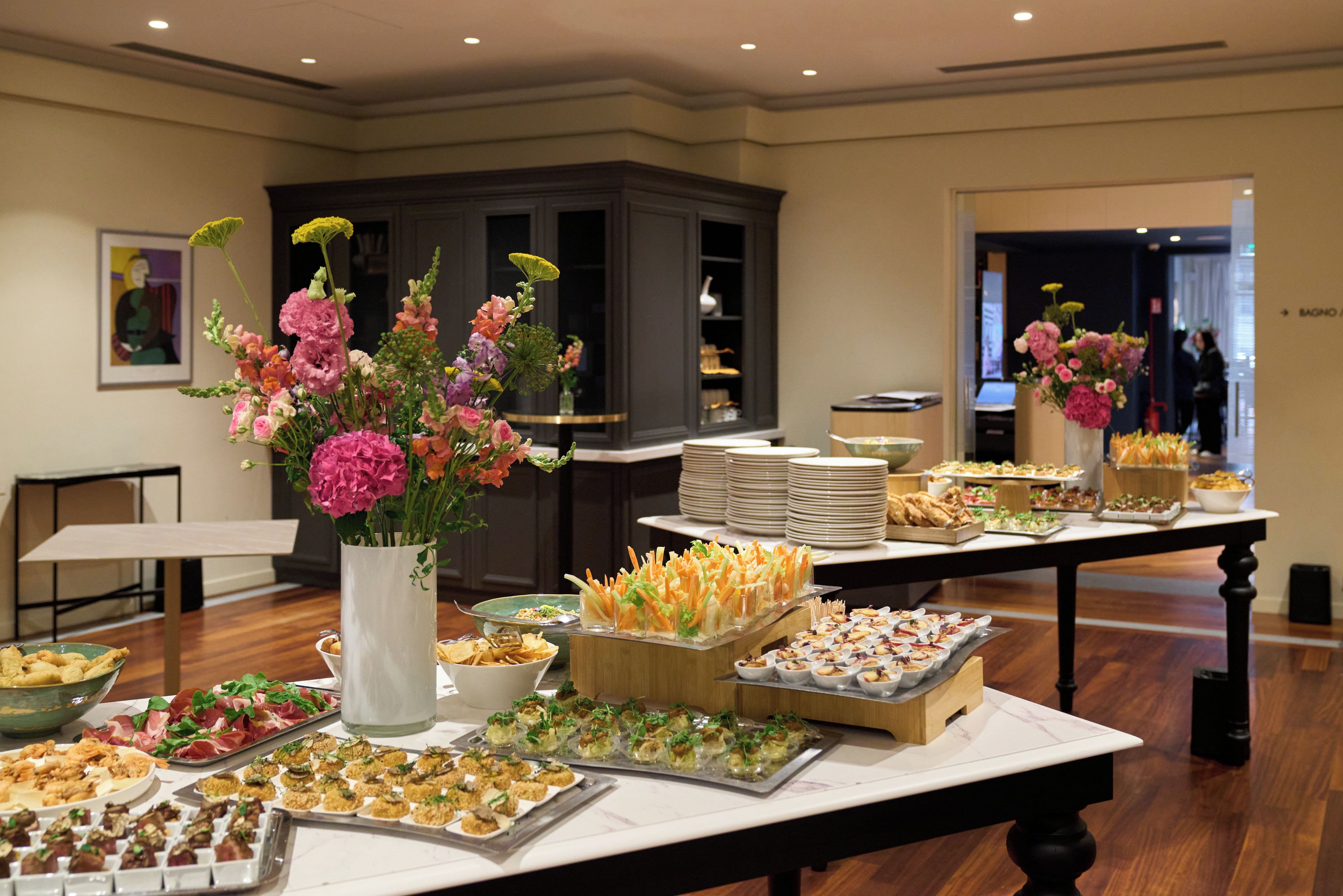 A buffet table with various food items and floral centerpieces.