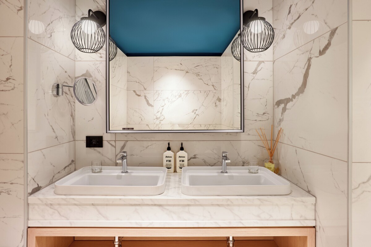 A bathroom with two sinks, a mirror, and two wall-mounted lights.