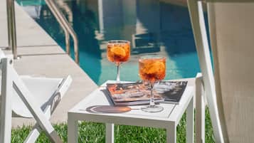 Escena junto a la piscina con dos vasos de una bebida y una revista sobre una mesita.